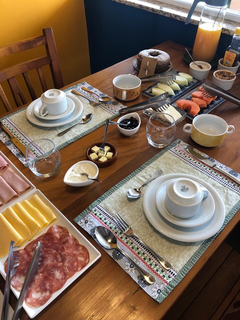 Mesa de café da manhã posta com frutas, bolos, frios e sucos